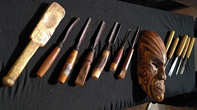 A row of wooden handled carving tools and a carved mask